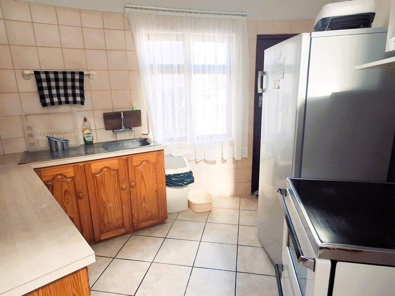 A functional kitchen featuring traditional wooden cabinetry, tiled backsplash, and tiled flooring, offering a practical layout with essential built-in fixtures.