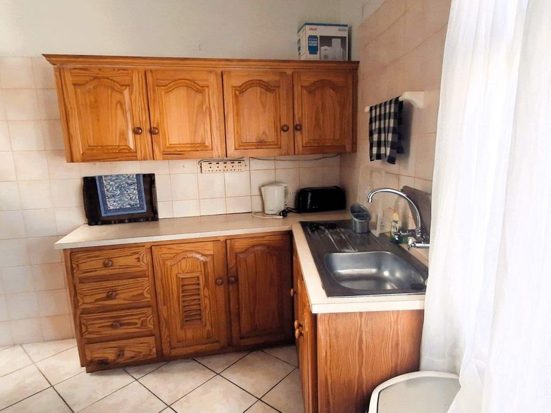A functional kitchen featuring traditional wooden cabinetry, tiled backsplash, and a stainless steel sink with a mixer tap.