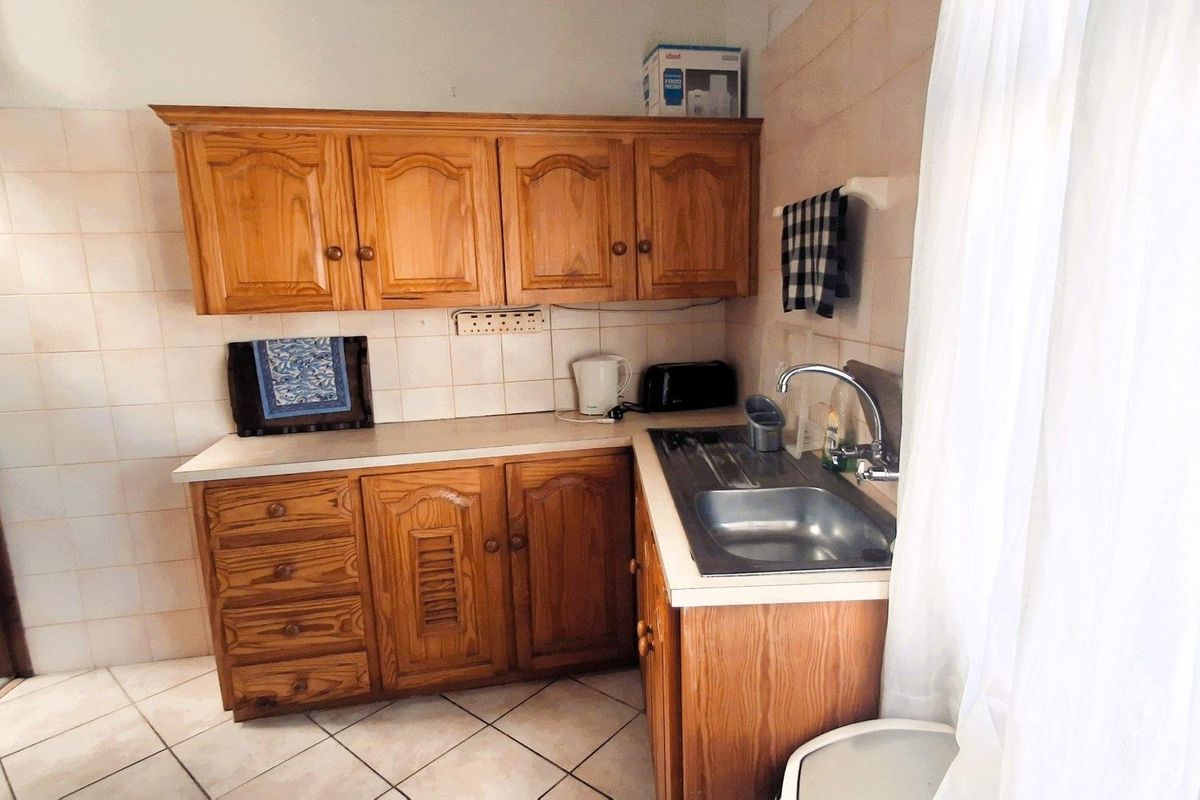 A functional kitchen featuring traditional wooden cabinetry, tiled backsplash, and a stainless steel sink with a mixer tap.