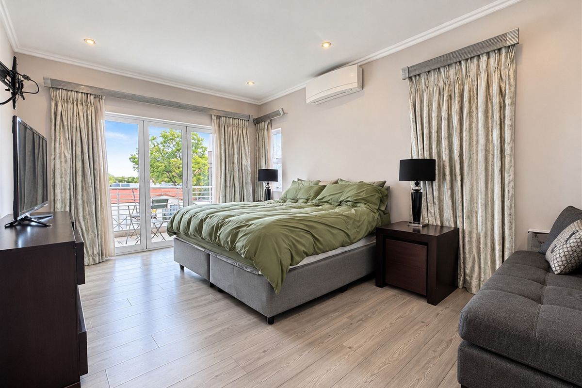 Spacious bedroom featuring light-toned laminate flooring, a wall-mounted split-system air conditioner, and direct access to a private balcony through sliding glass doors.