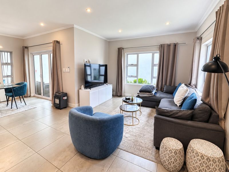 Spacious open-plan living and dining area featuring neutral tiled flooring, recessed lighting, and large windows providing ample natural light.