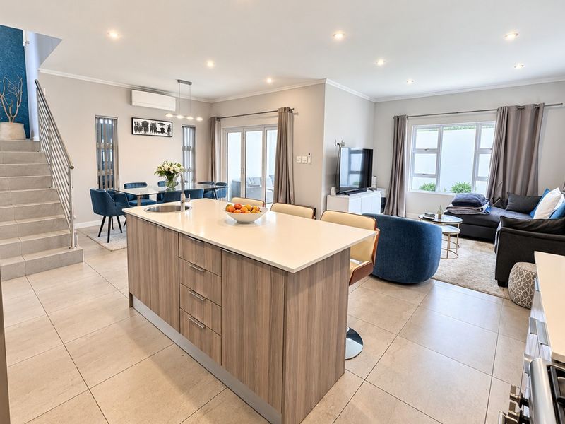 Spacious open-plan living area featuring a modern kitchen island, tiled flooring, recessed lighting, and a staircase with a sleek stainless steel balustrade.
