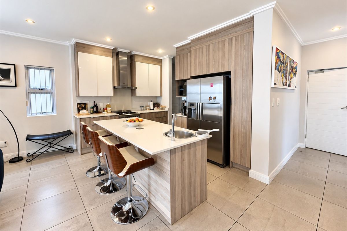 Modern kitchen featuring sleek wood-tone cabinetry, a central island with stone countertops, integrated appliances, and high-quality tiled flooring.