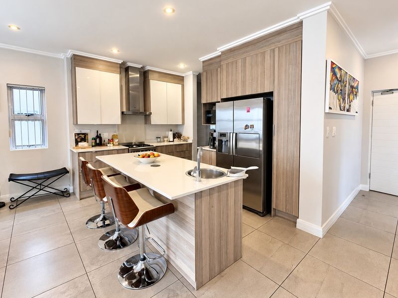Modern kitchen featuring sleek wood-tone cabinetry, a central island with stone countertops, integrated appliances, and high-quality tiled flooring.