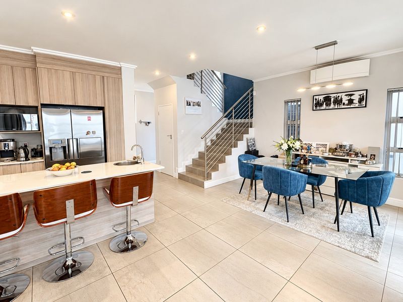 Modern open-plan living area featuring a contemporary kitchen with island, tiled flooring, and a staircase with a sleek metal balustrade.