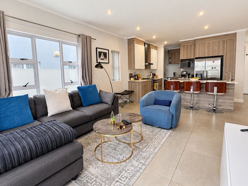 Modern open-plan living area featuring a contemporary kitchen with island seating, tiled floors, and abundant natural light from large windows.