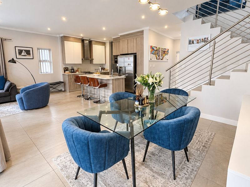 Modern open-plan living and dining area featuring a contemporary kitchen with island, tiled floors, and a sleek staircase with stainless steel balustrade.