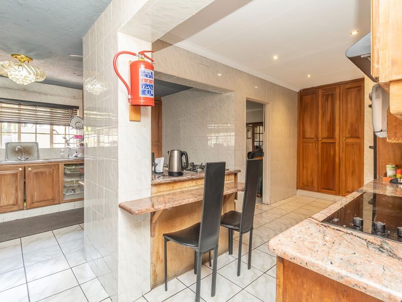Functional kitchen featuring granite countertops, built-in wooden cabinetry, tiled walls, and a breakfast bar area with integrated hob and extractor fan.