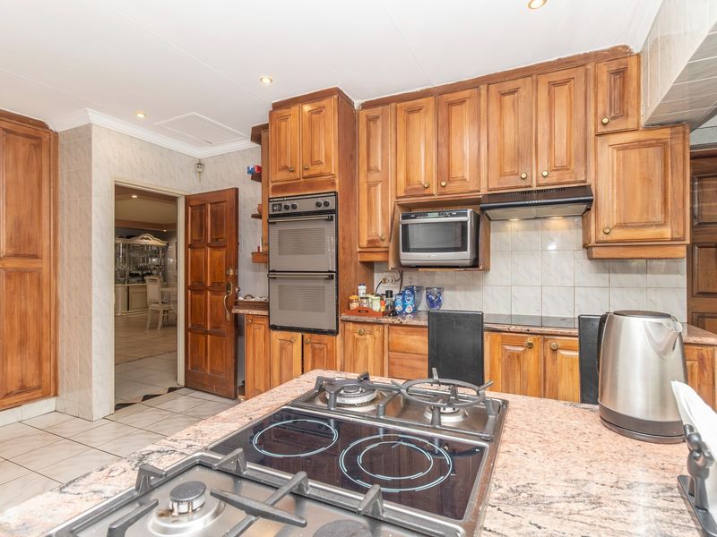 Traditional kitchen featuring wooden cabinetry, granite countertops, a built-in double oven, and a combined gas and electric hob on the central island.