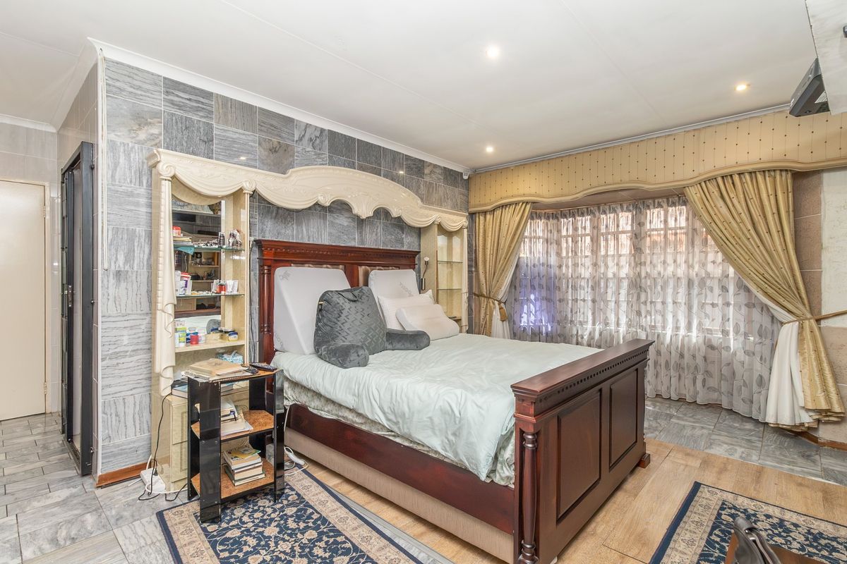 Spacious bedroom featuring stone-look wall tiling, recessed downlighting, and a built-in headboard unit, offering a unique aesthetic with potential for modern updates.
