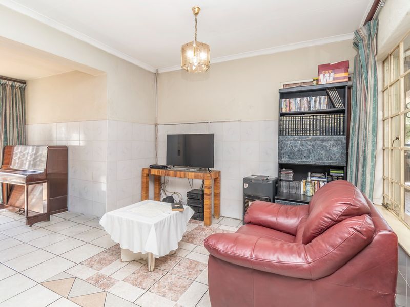 A living room featuring tiled flooring, wall tiling, and steel-framed windows, offering a dated interior space with potential for modernization.