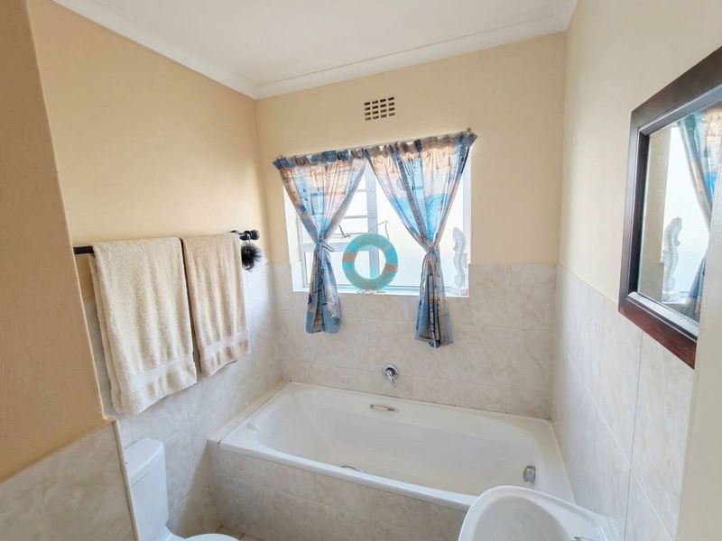 A functional bathroom featuring a built-in bathtub, tiled wall finishes, a toilet, and a washbasin, with natural light provided by a window.