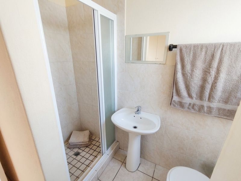 A functional bathroom featuring a pedestal washbasin, tiled walls and flooring, and a glass-enclosed shower unit.