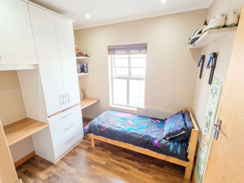 A well-maintained bedroom featuring built-in cabinetry, a integrated desk space, laminate flooring, and a window with a fitted blind.
