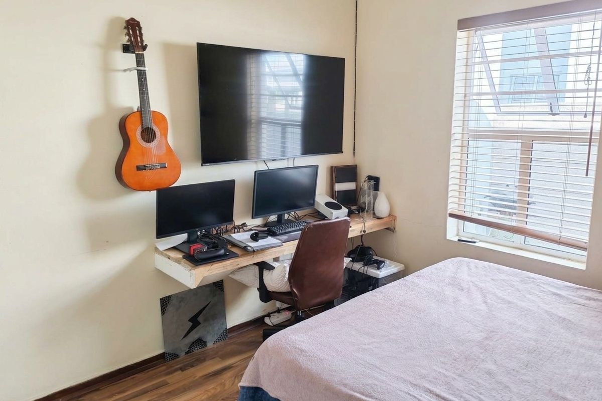 A functional bedroom featuring laminate flooring, venetian blinds, and a wall-mounted desk setup, offering a practical space for rest and work.