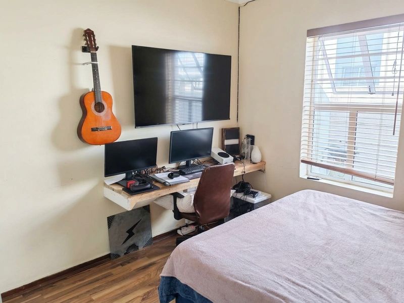 A functional bedroom featuring laminate flooring, venetian blinds, and a wall-mounted desk setup, offering a practical space for rest and work.