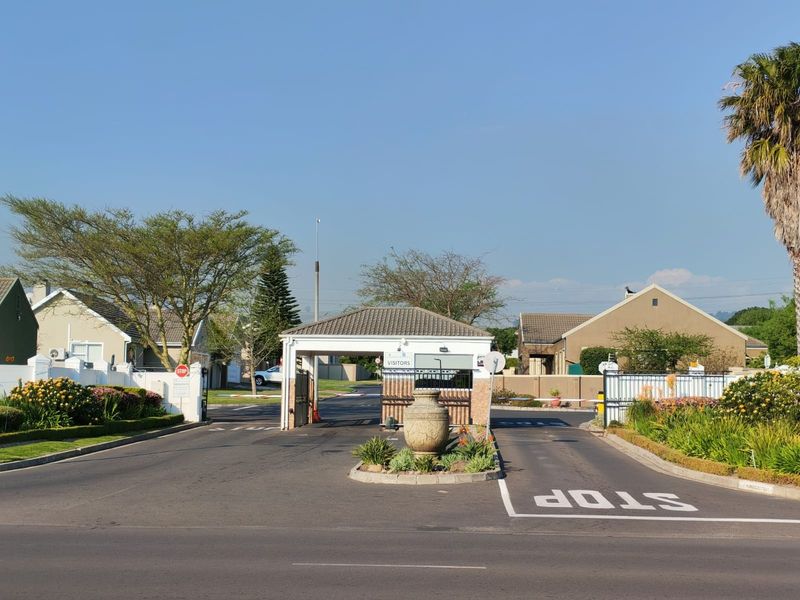 The entrance to the residential estate features a secure gatehouse with boom gates, well-maintained asphalt roads, and landscaped garden beds.