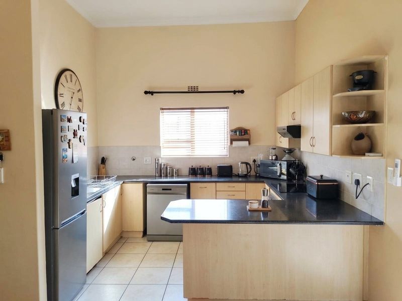 A functional kitchen featuring light wood-finish cabinetry, dark granite countertops, tiled flooring, and a tiled backsplash with a window for natural light.