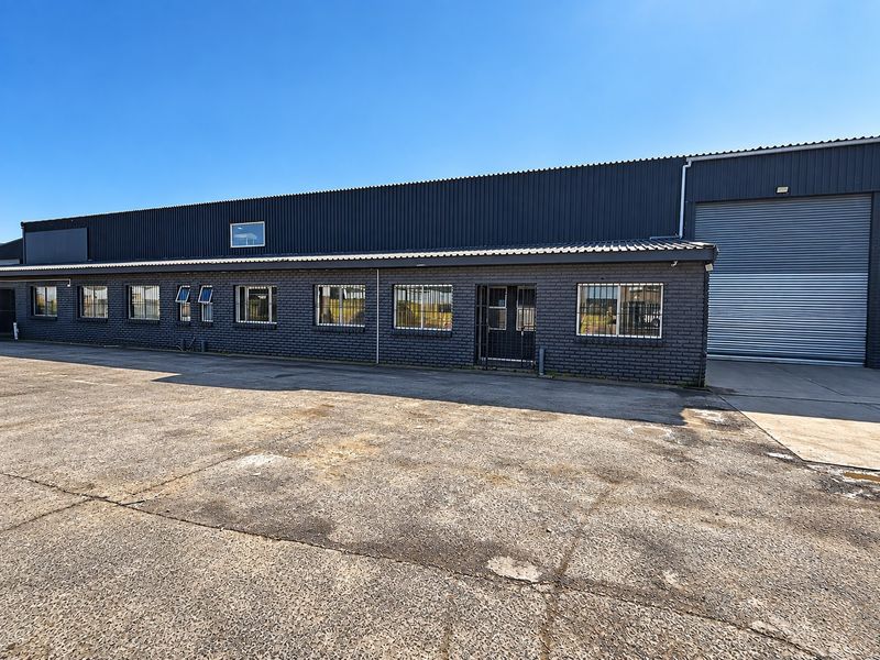 Industrial warehouse exterior featuring dark brick facade, corrugated metal cladding, large roller shutter door, and security-fitted windows with a concrete yard area.