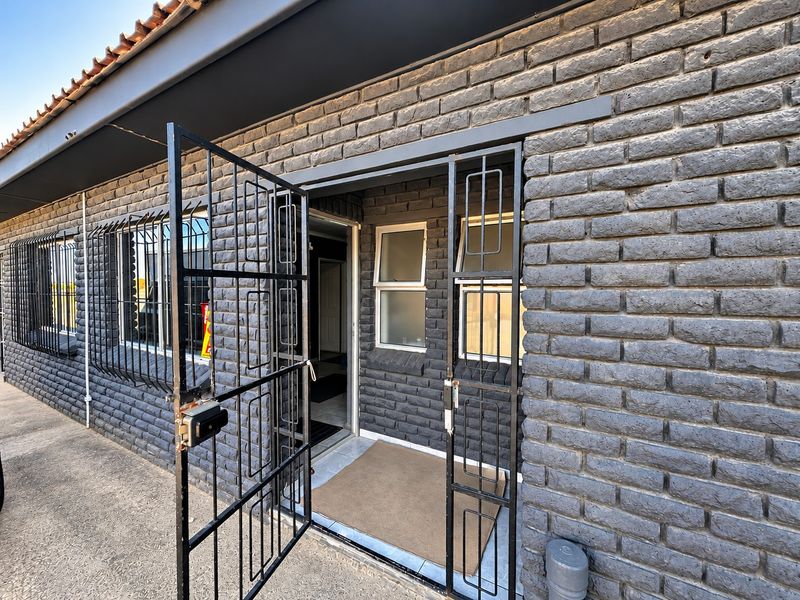 Exterior view of an industrial property featuring dark brickwork, security gates, and protective window bars.