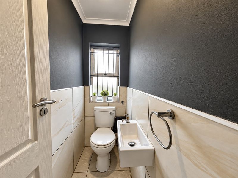 A compact, modern guest bathroom featuring tiled walls, a wall-mounted basin, and a toilet, finished with dark accent walls and security bars on the window.