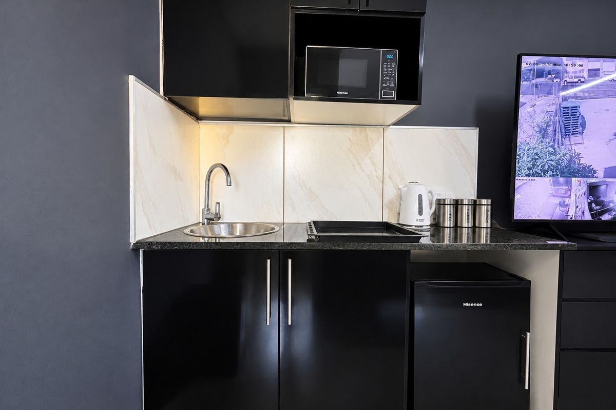 Compact kitchenette featuring modern black cabinetry, marble-look splashback, stainless steel sink, built-in microwave, and an under-counter fridge.