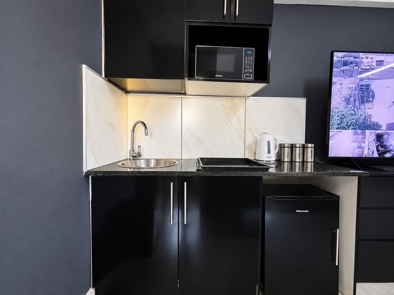 Compact kitchenette featuring modern black cabinetry, marble-look splashback, stainless steel sink, built-in microwave, and an under-counter fridge.
