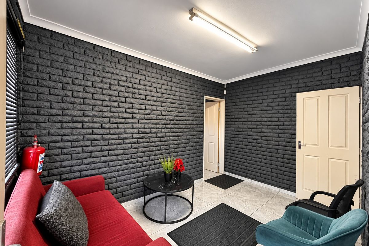 A functional office space featuring dark textured brick walls, neutral tiled flooring, and a bright overhead fluorescent light fixture.