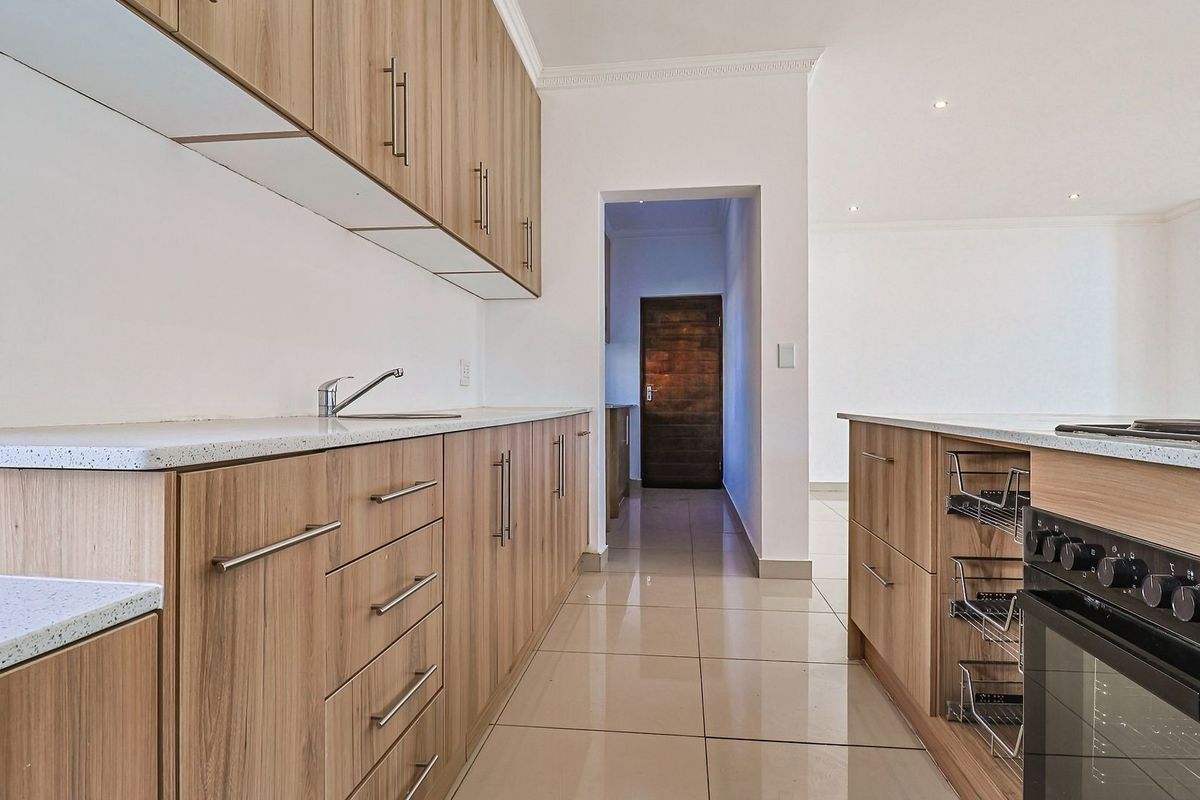 Modern kitchen featuring light wood-grain cabinetry, stone countertops, integrated oven and hob, and polished tiled flooring in a clean, open-plan layout.