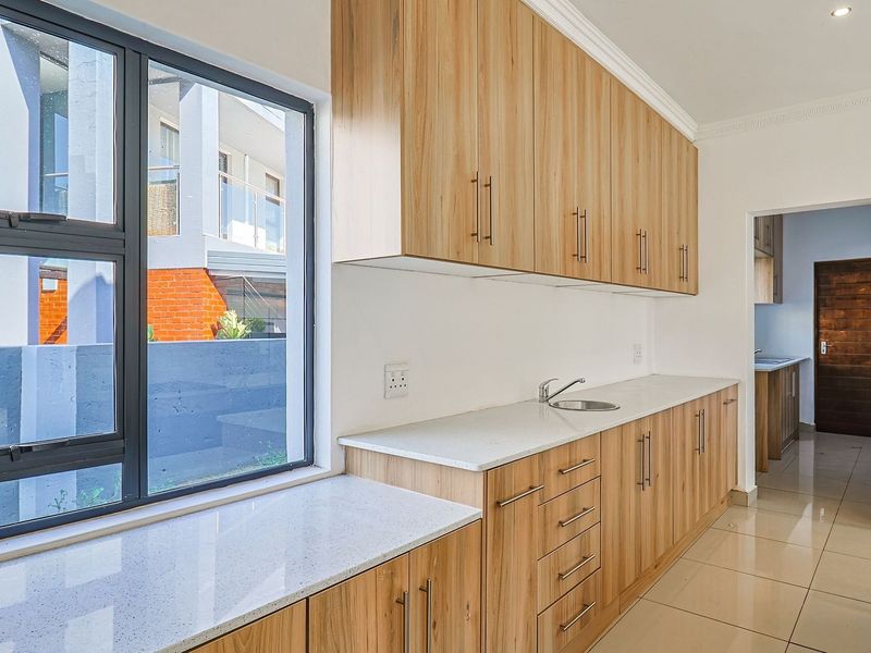 A clean, modern scullery featuring light wood-finish cabinetry, stone countertops, an undermount sink, and large windows providing ample natural light.