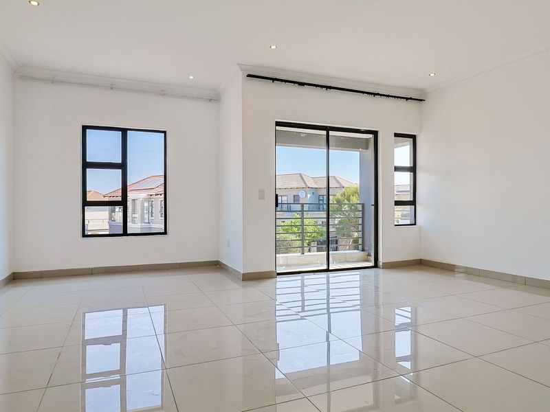 A bright, vacant living area featuring polished porcelain tiles, modern aluminium window frames, and a sliding glass door leading to an outdoor balcony.