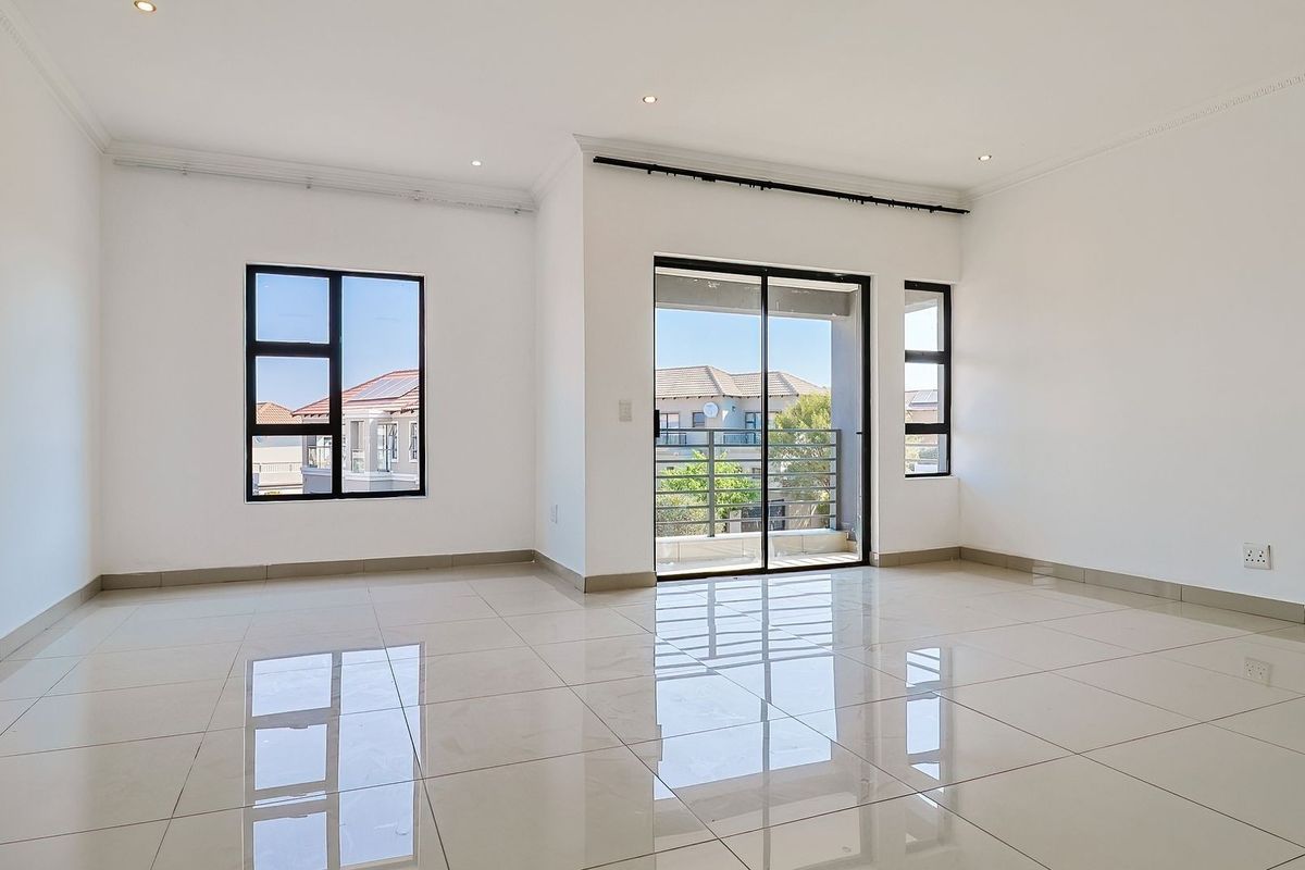 A bright, vacant living area featuring polished porcelain tiles, modern aluminium window frames, and a sliding glass door leading to an outdoor balcony.