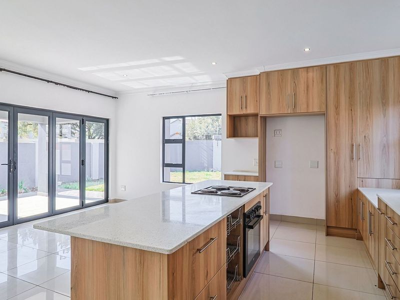 Modern open-plan kitchen featuring wood veneer cabinetry, stone countertops, a central island with a built-in hob and oven, and seamless access to the patio.