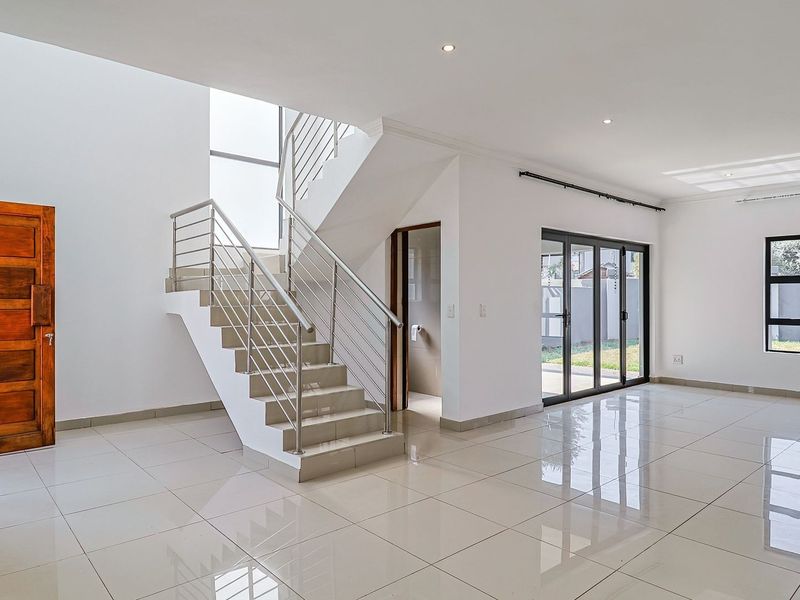 Spacious open-plan living area featuring polished tile flooring, a modern staircase with stainless steel balustrades, and large aluminium doors leading to the garden.