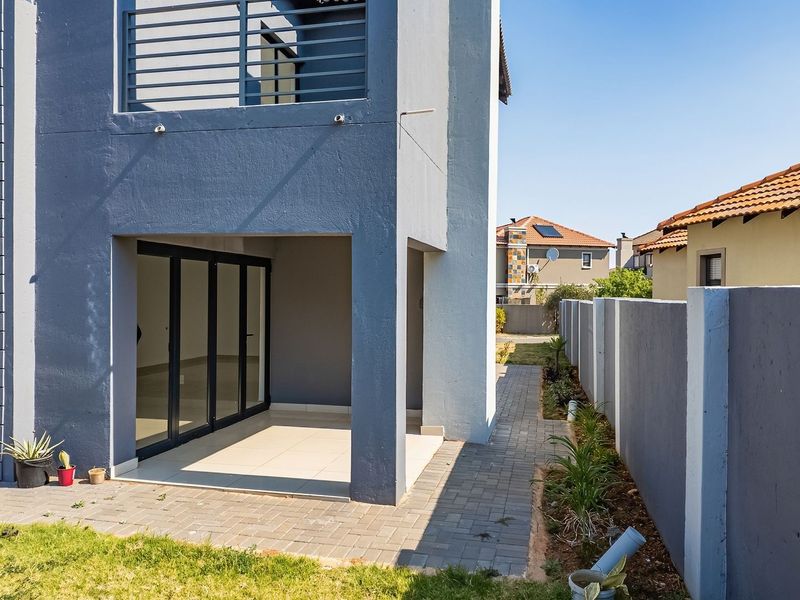 Rear view of the property featuring a covered patio with sliding glass doors, a paved walkway, and a secure boundary wall.