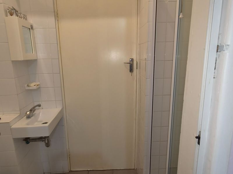 A compact bathroom featuring tiled walls, a wall-mounted basin, and a shower enclosure, presenting a functional space in need of modernization.