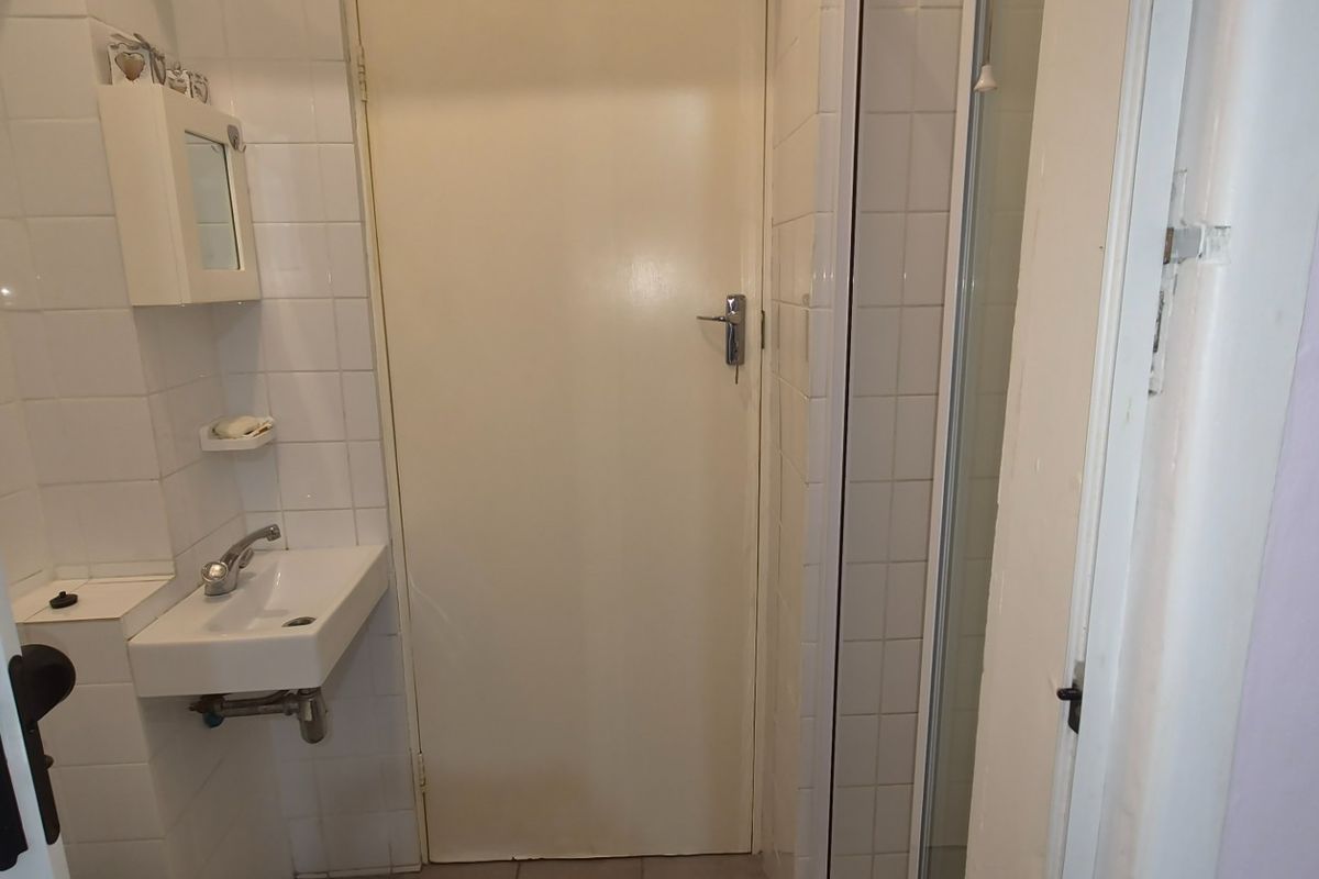 A compact bathroom featuring tiled walls, a wall-mounted basin, and a shower enclosure, presenting a functional space in need of modernization.