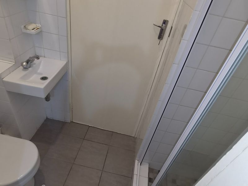 A compact bathroom featuring a wall-mounted basin, toilet, and a glass-enclosed shower with neutral tiled finishes.