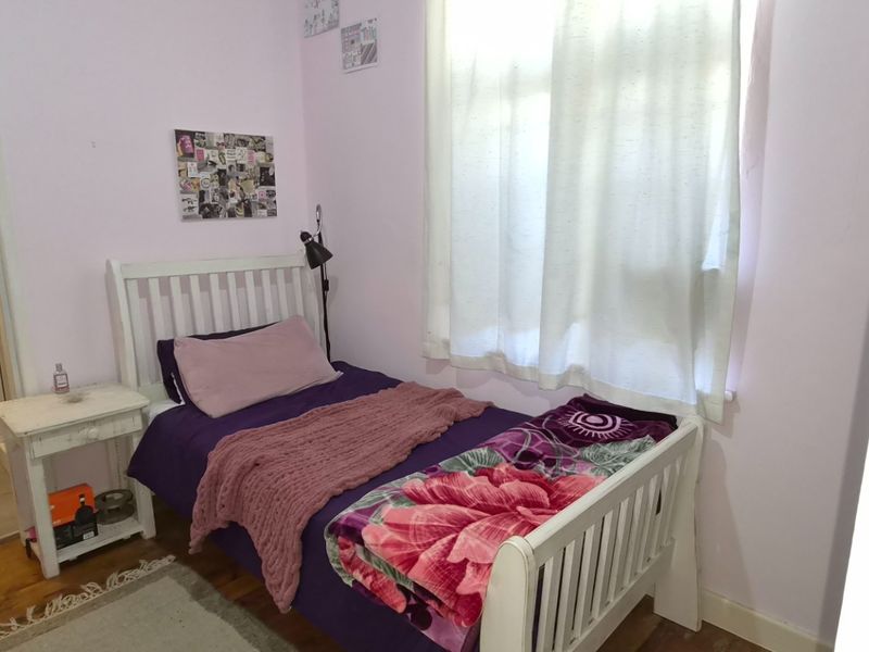 A compact bedroom featuring timber flooring and a window, providing a functional space with neutral wall finishes.
