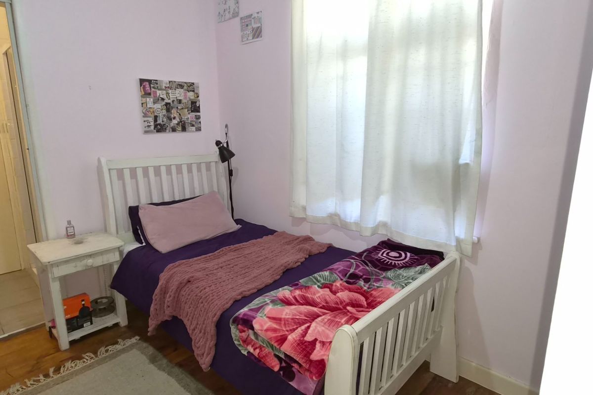 A compact bedroom featuring timber flooring and a window, providing a functional space with neutral wall finishes.