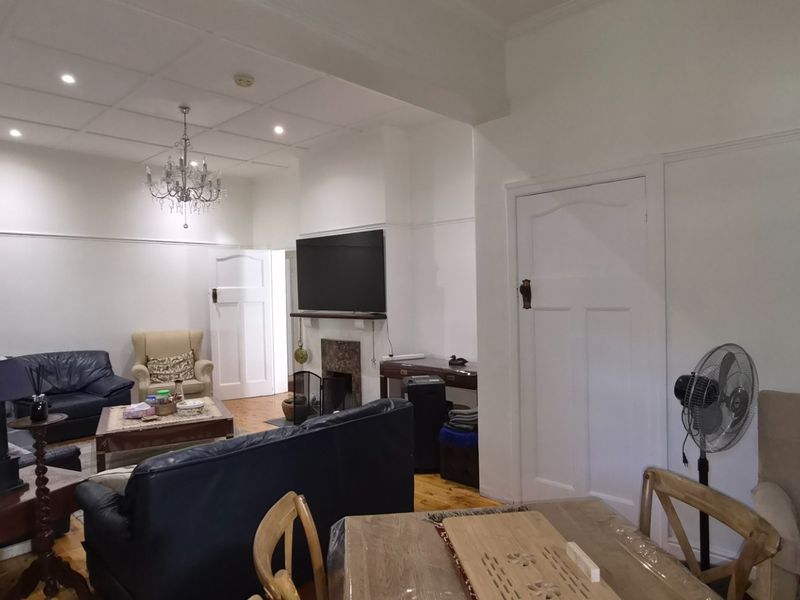 Spacious open-plan living and dining area featuring timber flooring, a fireplace, and classic architectural details including a panelled ceiling and picture rails.