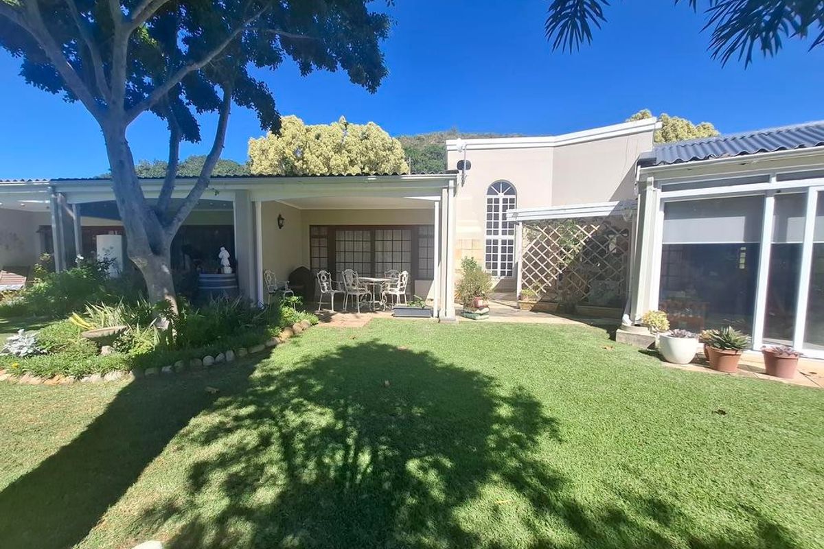 A well-maintained rear exterior view featuring a covered patio area, landscaped garden, and mature trees, providing a pleasant outdoor living space.