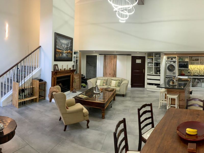 Spacious open-plan living area featuring a double-volume ceiling, fireplace, staircase, and a modern kitchen with a central island and integrated cabinetry.
