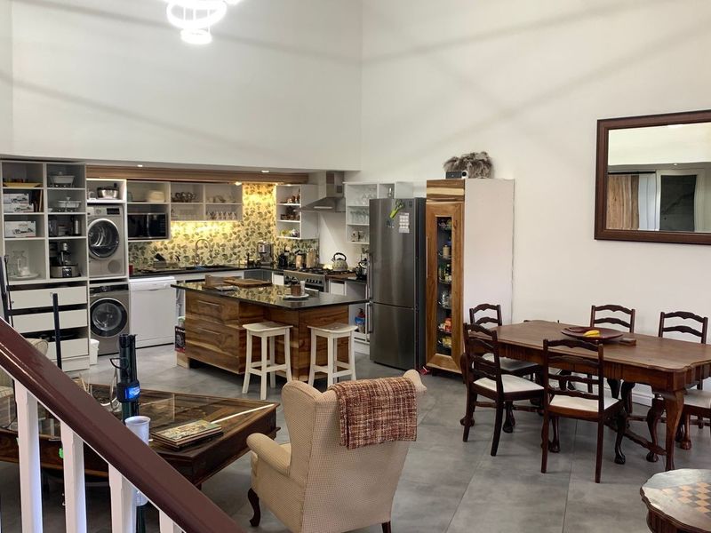 Spacious open-plan living and dining area featuring a modern kitchen with a central island, double-volume ceilings, and tiled flooring throughout.