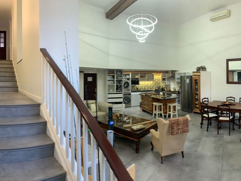 Spacious open-plan living area featuring a modern kitchen with island, tiled flooring, high ceilings with exposed beams, and a staircase leading to the upper level.
