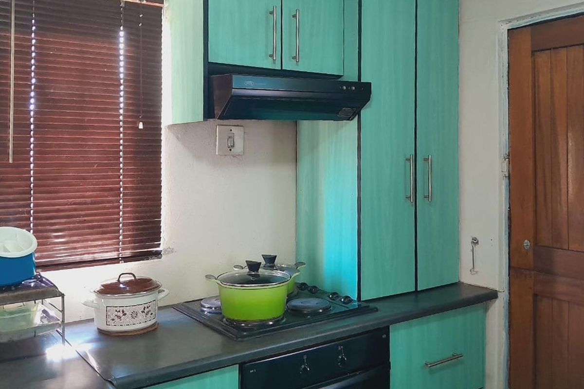 A compact kitchen featuring teal cabinetry, a built-in hob, oven, and extractor fan, with a wooden door and window blinds.