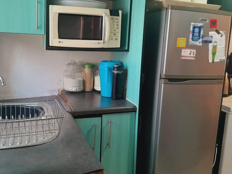 A compact kitchen area featuring teal cabinetry, dark laminate countertops, a stainless steel sink, and a built-in microwave space.