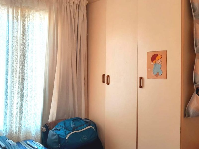 A bedroom featuring built-in cupboards and natural light from a window with curtains.