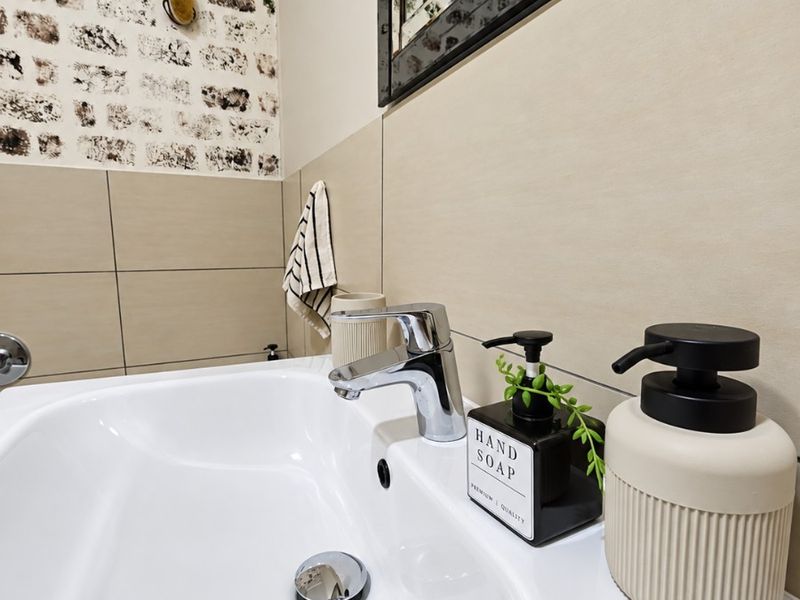 A modern bathroom vanity area featuring a clean white basin, chrome mixer tap, and decorative tiled wall finish.