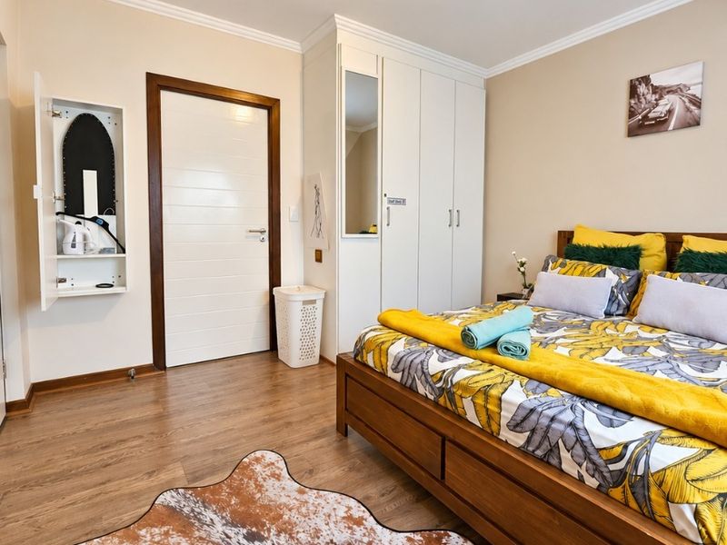 A well-maintained bedroom featuring laminate flooring, built-in wardrobes with a mirrored panel, and a wall-mounted ironing station.